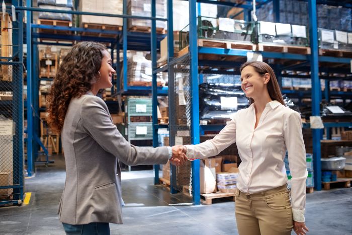 two-businesswomen-shaking-hands-warehouse