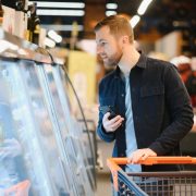 supermarket-handsome-man-uses-smartphone-looks-nutritional-value-canned-goods-he-s-standing-with-shopping-cart-canned-goods-section